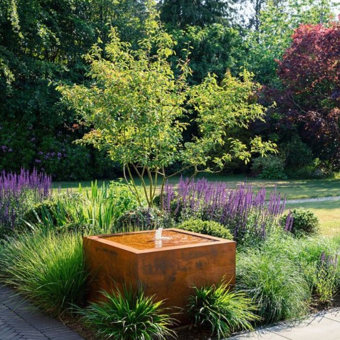 Urban Square Fountain positioned amidst vibrant plants and trees, complementing the landscape with its modern square design.